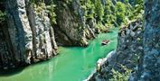 Eine malerische Schlucht mit steilen Felsen und klarem grünem Wasser. Ein Boot fährt ruhig durch die Landschaft, umgeben von üppigem Grün.