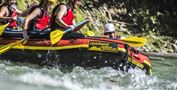 Eine Gruppe von Raftingfahrern paddelt in einem bunten Schlauchboot auf einem rauschenden Fluss. Alle tragen Helme und Schwimmwesten für Sicherheit.