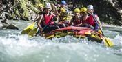 Eine Gruppe von sechs Personen paddelt in einem Raft auf einem wildem Fluss. Alle tragen Schwimmwesten und Helme und haben Spaß bei ihrem Abenteuer.