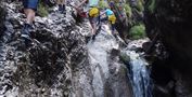 Gruppen von Menschen klettern an einer Felswand in einer Schlucht. Im Hintergrund fließt ein kleiner Wasserfall.