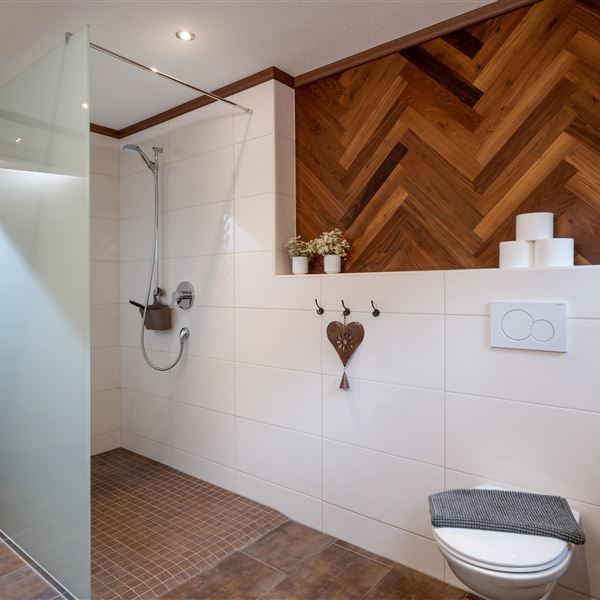 2. Foto zum 2. Badezimmer im Erdgeschoß: Ein modernes Badezimmer mit einer gläsernen Duschwand und einer Holzverkleidung. Die Ausstattung umfasst eine Toilette und dekorative Elemente wie Pflanzen.