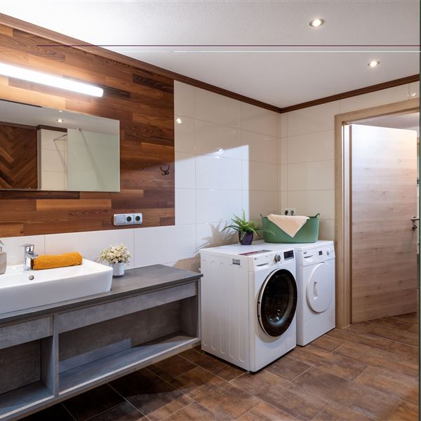 Ein modernes Badezimmer mit einer Waschmaschine, Trockner und einem eleganten Waschbecken. Die Holzverkleidung und der helle Raum sorgen für eine einladende Atmosphäre.