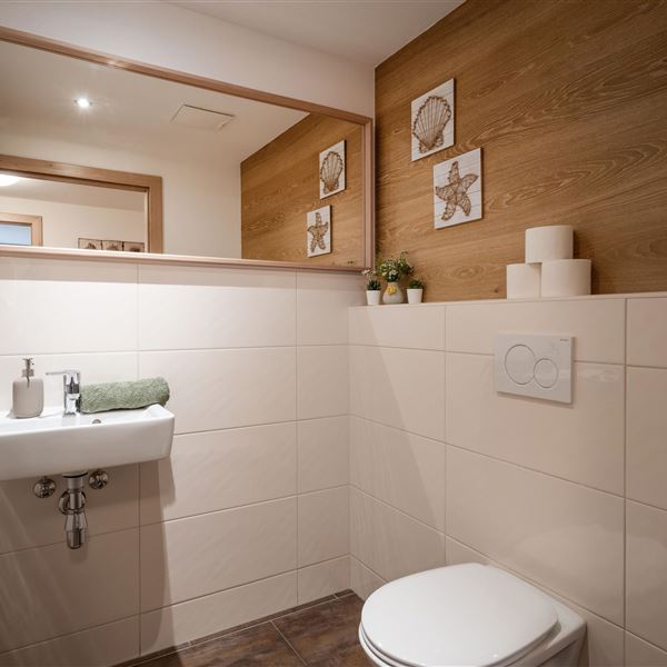 Eine moderne Toilette mit hellem, neutralem Design. Es enthält eine kleine Waschgelegenheit, eine Toilette und dekorative Elemente aus Holz.