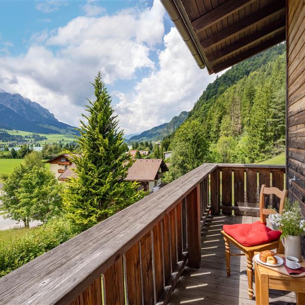 Ein Balkon mit Blick auf grüne Wiesen und majestätische Berge. Ein kleiner Tisch mit einem roten Kissen , ein Buch, eine Tasse Kaffee steht bereit zum Entspannen.