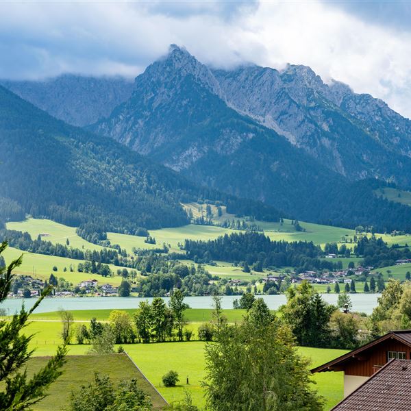 Eine malerische Landschaft mit grünen Wiesen und majestätischen Bergen im Hintergrund. Der Himmel ist leicht bewölkt, was eine ruhige Atmosphäre schafft.