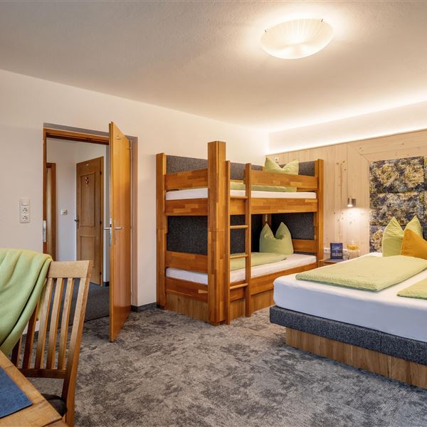 Sie sehen hier das dritte Schlafzimmer im Obergeschoß, 2026 renoviert,  mit einem großen Bett (200x210) und einem gemustertem Kopfteil sowie einem Eiche-Vollholz-Stockbett 90x200. Der Raum ist hell und gemütlich, mit Seeblick,  einer Balkontür und Balkonzugang, Fliegengitter, Verdunkelungsvorhängen und  Eichenmöbeln.