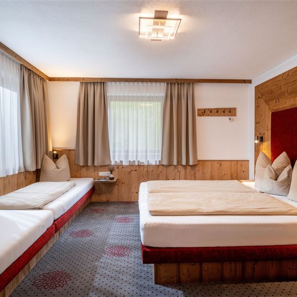 Ein gemütliches Schlafzimmer mit einem Doppelbett 200x210, zwei Einzelbetten und hellem Holzdekor. Große Fenster mit Seeblick und Waldblick sorgen für viel Tageslicht und eine entspannte Atmosphäre. Fliegengitter und Verdunkelungsvorhänge sind vorhanden