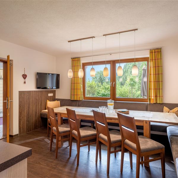 Eine helle und einladende Küche mit einem großen Esstisch und Stühlen. Große Fenster bieten einen Blick in den Garten und im Winter auf den Rutschhang für die Kinder