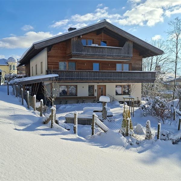 Ein gemütliches Ferienhaus im Schnee mit einem klaren blauen Himmel. Die Umgebung ist friedlich und winterlich, vor dem Küchenfenster ist ein Hang, welcher ideal zum Rutschen für Kinder geeignet ist.  Einige Rutschteller haben wir dafür im Sonnhof für Sie.