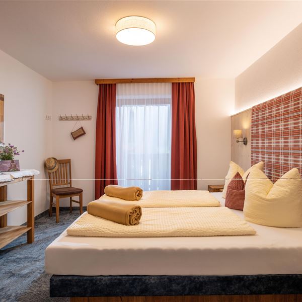 Sie sehen hier  das zweite Schlafzimmer im Obergeschoß, 2026 renoviert,  mit einem großen Bett (200x210) und einem karierten Kopfteil. Der Raum ist hell und gemütlich, mit einer Balkontür und Balkonzugang, Fliegengitter, Verdunkelungsvorhängen und  Eichenmöbeln.